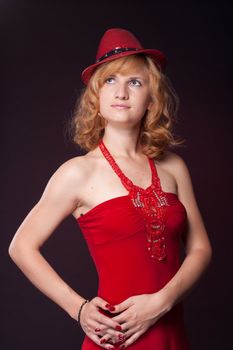 Red-haired girl in a red dress and red hat. Studio photography