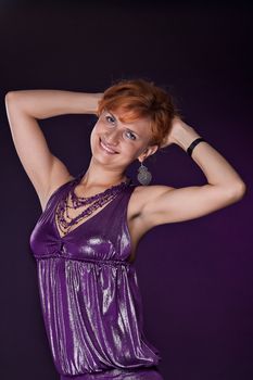  Red-haired girl in a purple dress on a dark background. Studio photography