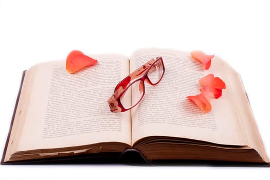 The open book with glasses and rose petals on white background