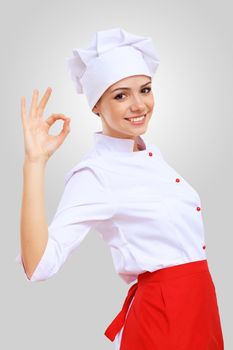 Young female chef in red apron against grey background