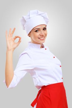 Young female chef in red apron against grey background