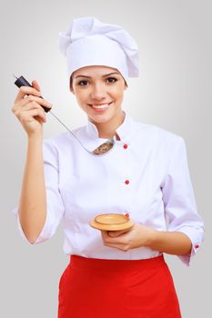 Young female chef in red apron against grey background