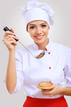 Young female chef in red apron against grey background