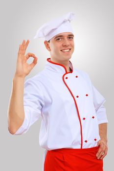 Young male chef in red apron against grey background