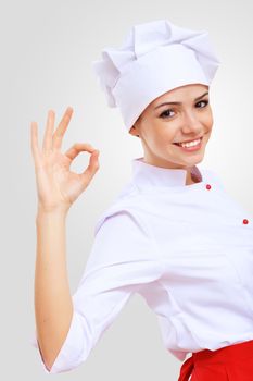 Young female chef in red apron against grey background