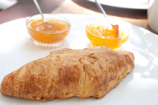 Large croissant on a plate with a portion of jam in a cafe shooting