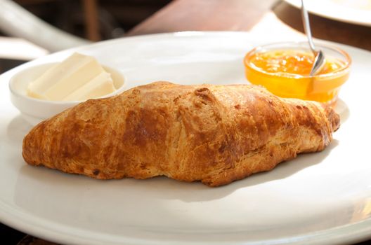 Large croissant on a plate with a portion of jam in a cafe shooting