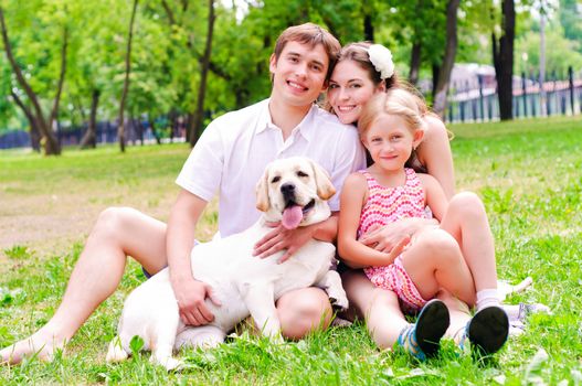 Happy young family with Labrador is resting in the park