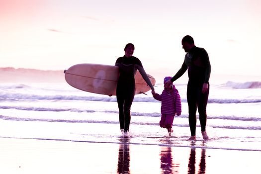 Female surfer and her familly walking in the beach at the sunset