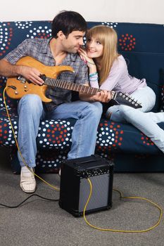 Cheerful couple resting on a sofa with electric guitar