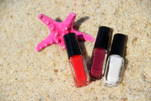 Three nail polish bottle on the beach and pink starfish;