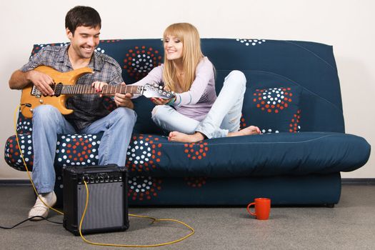 Young beautiful couple resting at home and playing electric guitar