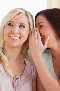 Smiling woman telling her friend a secret in a living room