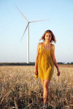 Lady walking in the field with wind power generator on background