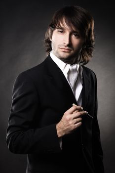 Handsome man in elegant clothing with cigar against black background