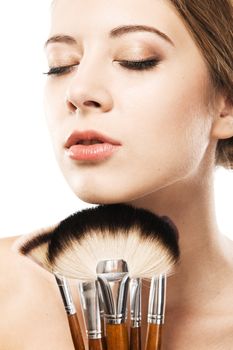 Closeup portrait of a beautiful young woman with makeup brushes 