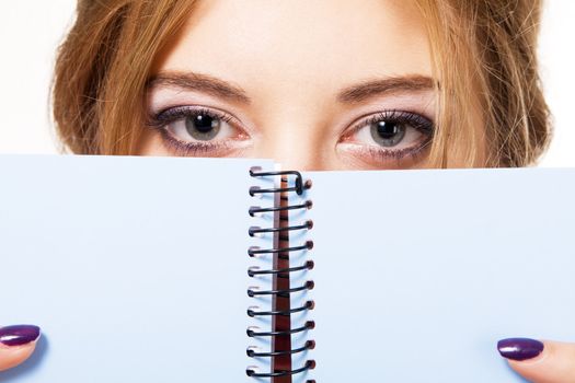 Lovely girl hiding behind notebook, white background