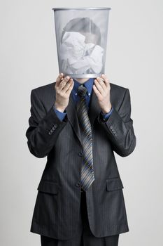 Young man holdin a trash bin against his head, neutral background