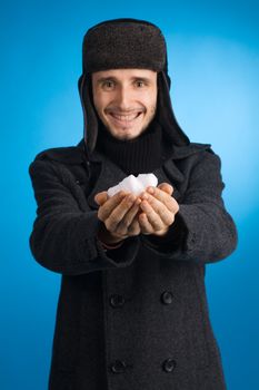 Handsome young man in winter clothing holding out a handful of snow