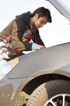 Car driver examining the car's engine on a parking 