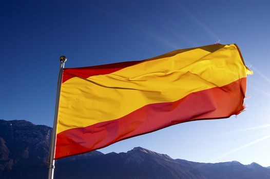 Red and yellow national spanish flag blowing in the wind with blue sky