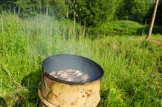 fish smoking for food in retro rusty barrel. Rural food prepare.