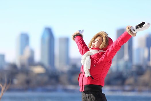 City winter woman happy standing excited and elated with arms raised in joy. Beautiful young woman and Montreal City skyline, Quebec, Canada.