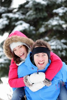 Young excited happy winter couple doing piggyback having fun outside in winter snow forest landscape. Happy young interracial couple, Caucasian man, Asian woman.