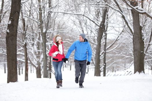 Couple walking and running in winter forest happy and joyful holding hands on romantic date in winter snow forest landscape. Cheerful interracial young couple, Asian woman, Caucasian man.