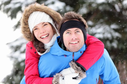 Winter couple happy doing piggyback in winter snow forest. Cheerful smiling young interracial couple having fun outside piggybacking. Asian woman, Caucasian man.