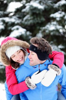 Happy winter couple having fun doing piggyback in snow winter landscape outside in forest. Beautiful young interracial couple piggybacking.