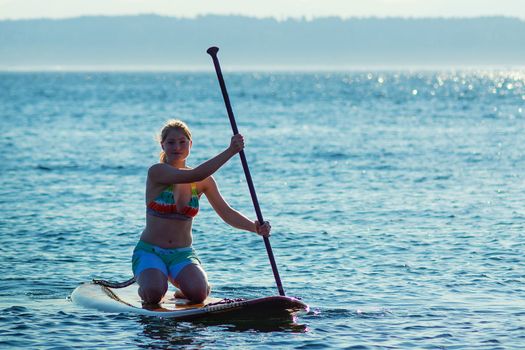 Woman paddling stand up paddle board while kneeling.