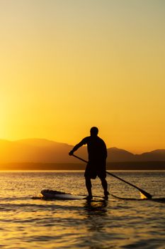 Man paddling stand up paddle board at sunset with mountains in background.