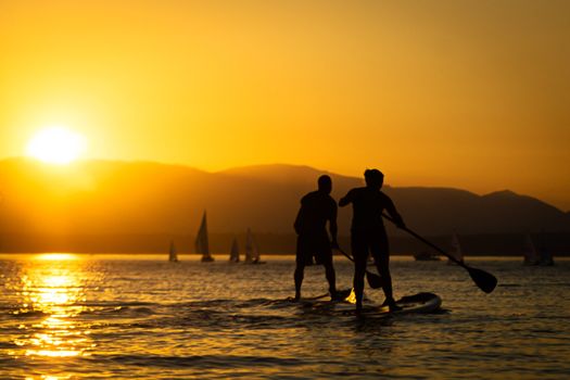 Couple paddling stand up paddle boards at sunset with mountains in background.