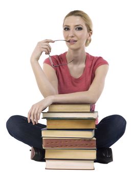 Female student biting her eye glasses while sitting with a pile of books