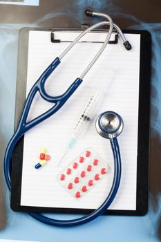 Note pad and blister strip with pills and blue stethoscope on a blue and dark background