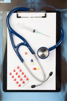 Note pad and blister strip with medicine and blue stethoscope on a blue and dark background