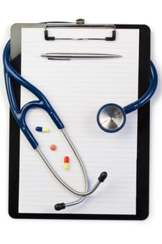 Note pad and stethoscope with pen at the top and pills on a white background