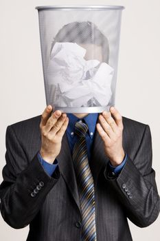 Young man holdin a trash bin against his head, neutral background