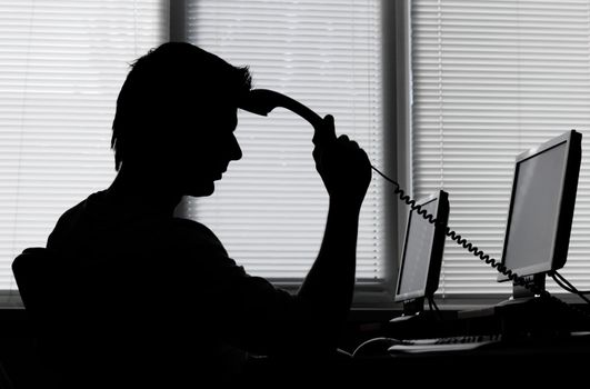 Business man pondering over the phone, in backlight