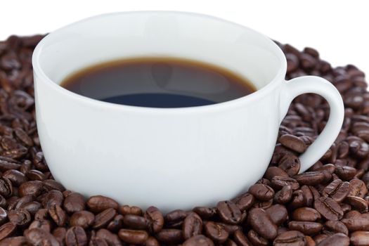 White cup of coffee surrounded with coffee beans on a white background