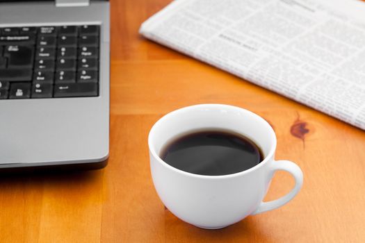 White cup of coffee with laptop and newspaper on a desk