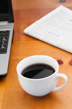 White cup of coffee with laptop and newspaper on a desk