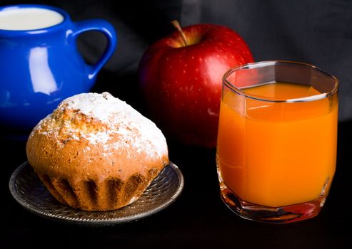 Muffin, apple and orange juice on dark background