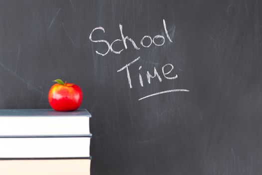 Stack of books with a red apple and a blackboard with "school time" written on it