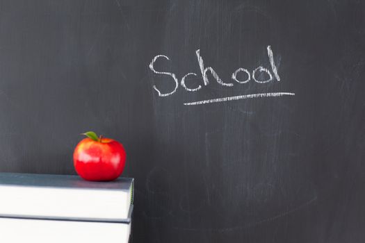 Stack of books with a red apple and a blackboard with "school" written on it