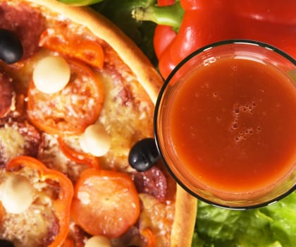 Closeup picture of a pizza with vegetables and glass of tomato juice