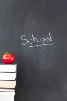 Stack of books with a red apple and a blackboard with "school" written on it