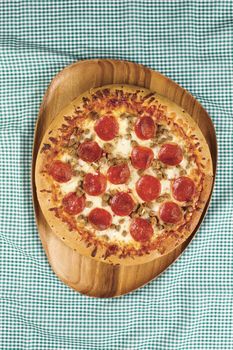 Overhead shot of a pepperoni pizza on wooden plate.