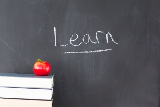 Stack of books with a red apple and a blackboard with "learn" written on it